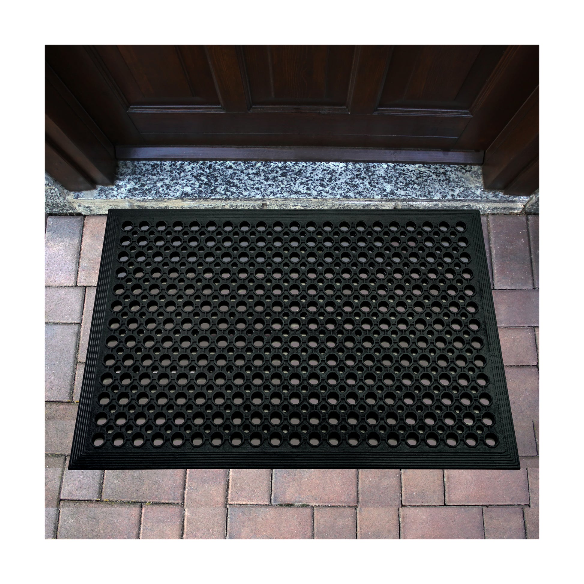 All Weather Outdoor Entrance Mat with honeycomb design positioned outside by a doorway in a lifestyle setting