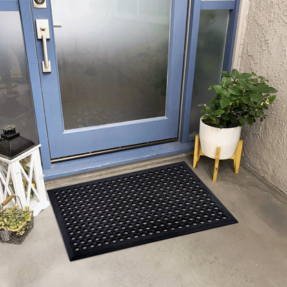 Black doormat in front of a blue door with a plant and small table nearby.
